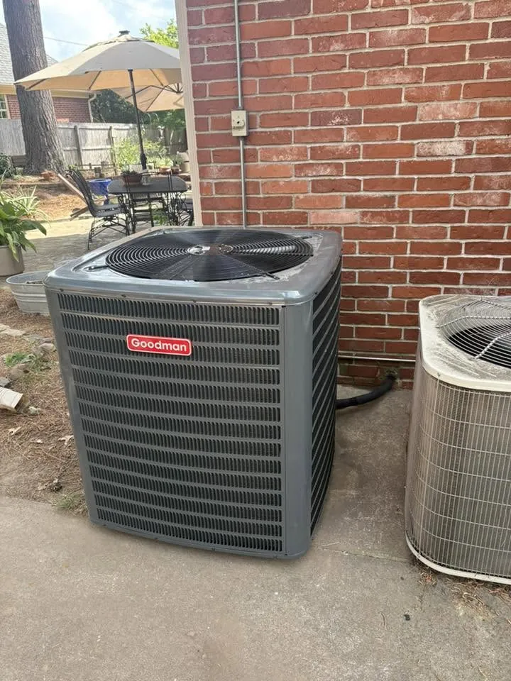 Goodman condenser on a pad beside a brick wall and patio